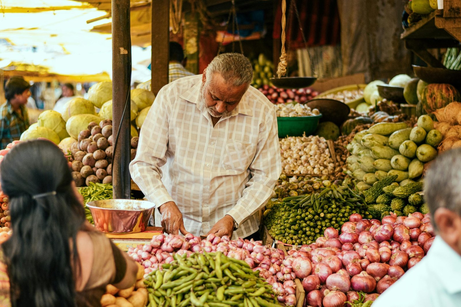 A senior male vendor organizing a colorful array of fresh produce in a bustling outdoor market.